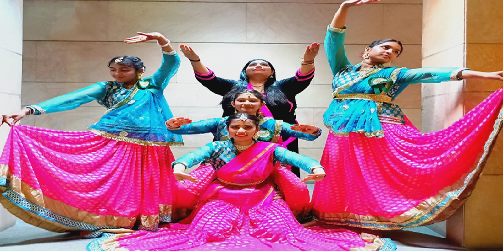 Kathak dancers in pink and teal costumes striking a group pose